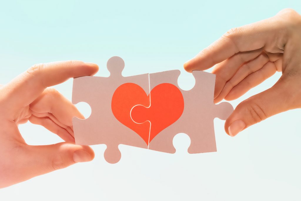 Manos de una pareja forman un corazón con dos piezas de puzle