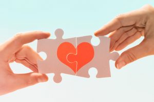 Manos de una pareja forman un corazón con dos piezas de puzle
