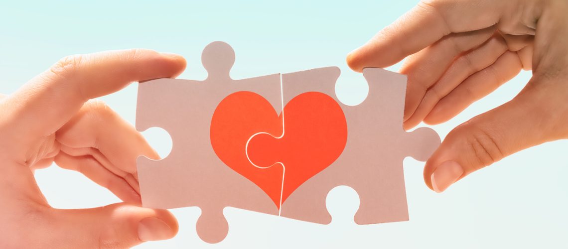 Manos de una pareja forman un corazón con dos piezas de puzle